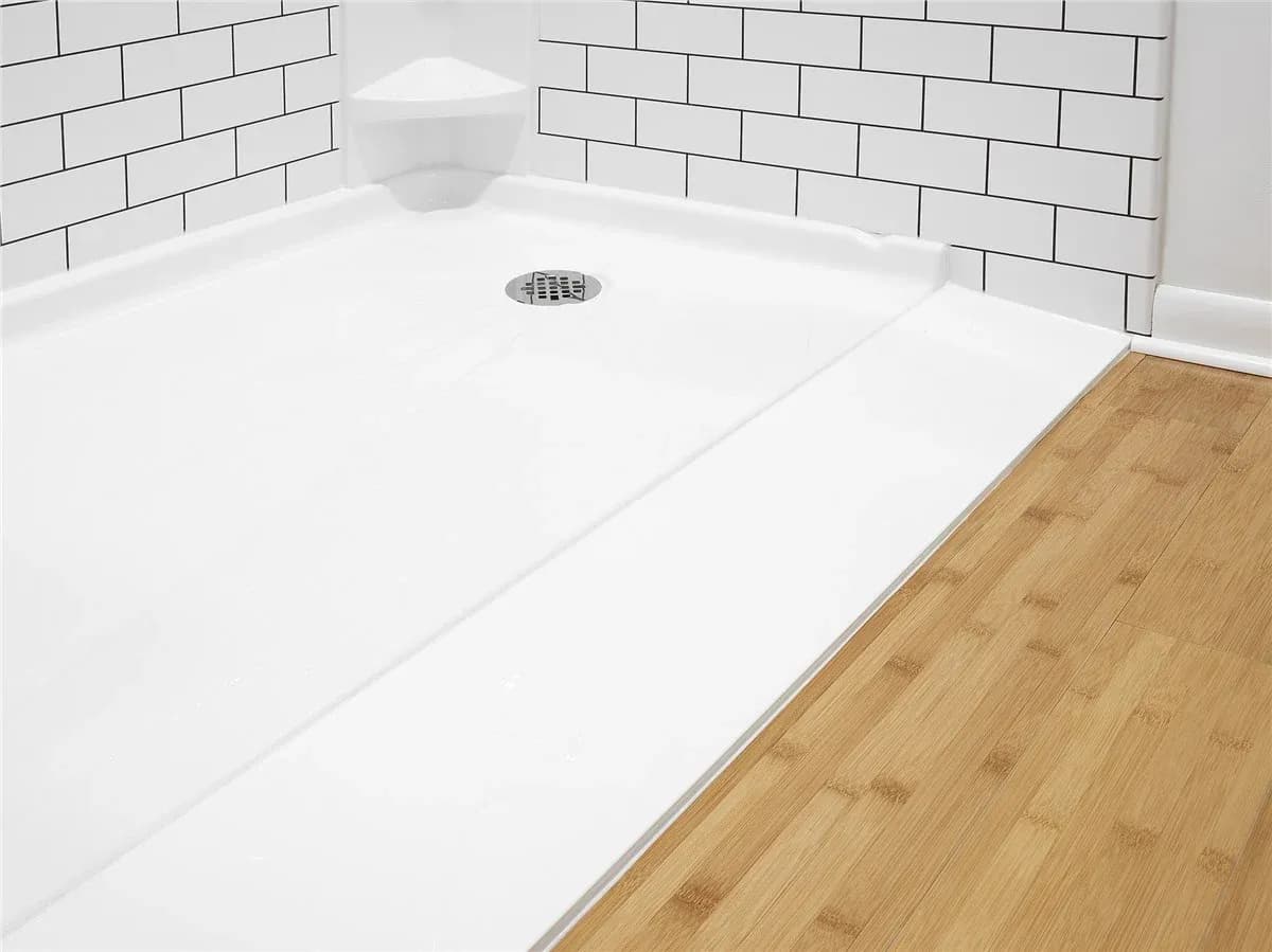White tile shower base with drain and bench seat, bordered by subway tile walls and bamboo flooring