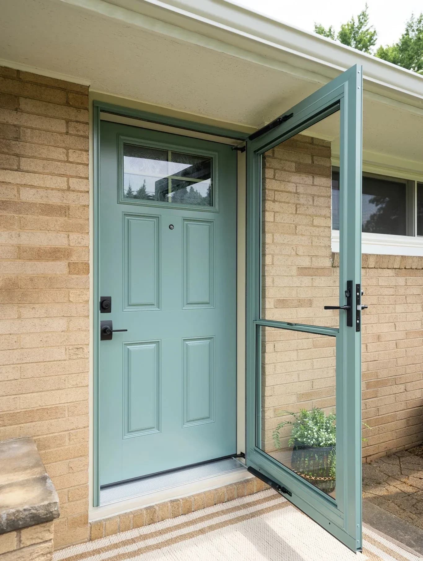 Mint green front door with window and matching open storm door on brick house exterior with covered entryway