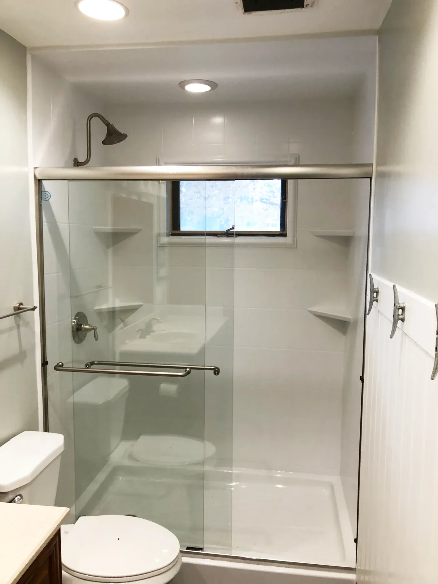 Modern bathroom with glass-enclosed walk-in shower featuring built-in shelves and rainfall showerhead, adjacent white toilet and vanity