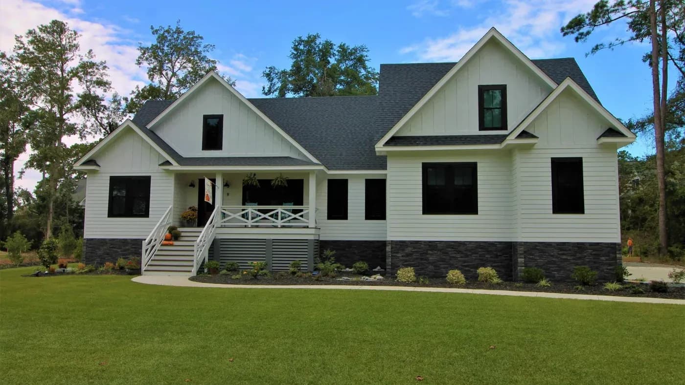 Modern two-story home with white siding, dark shutters, and elevated foundation on manicured lawn surrounded by trees