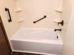 Newly installed white bathtub with beige surround and dark hardware