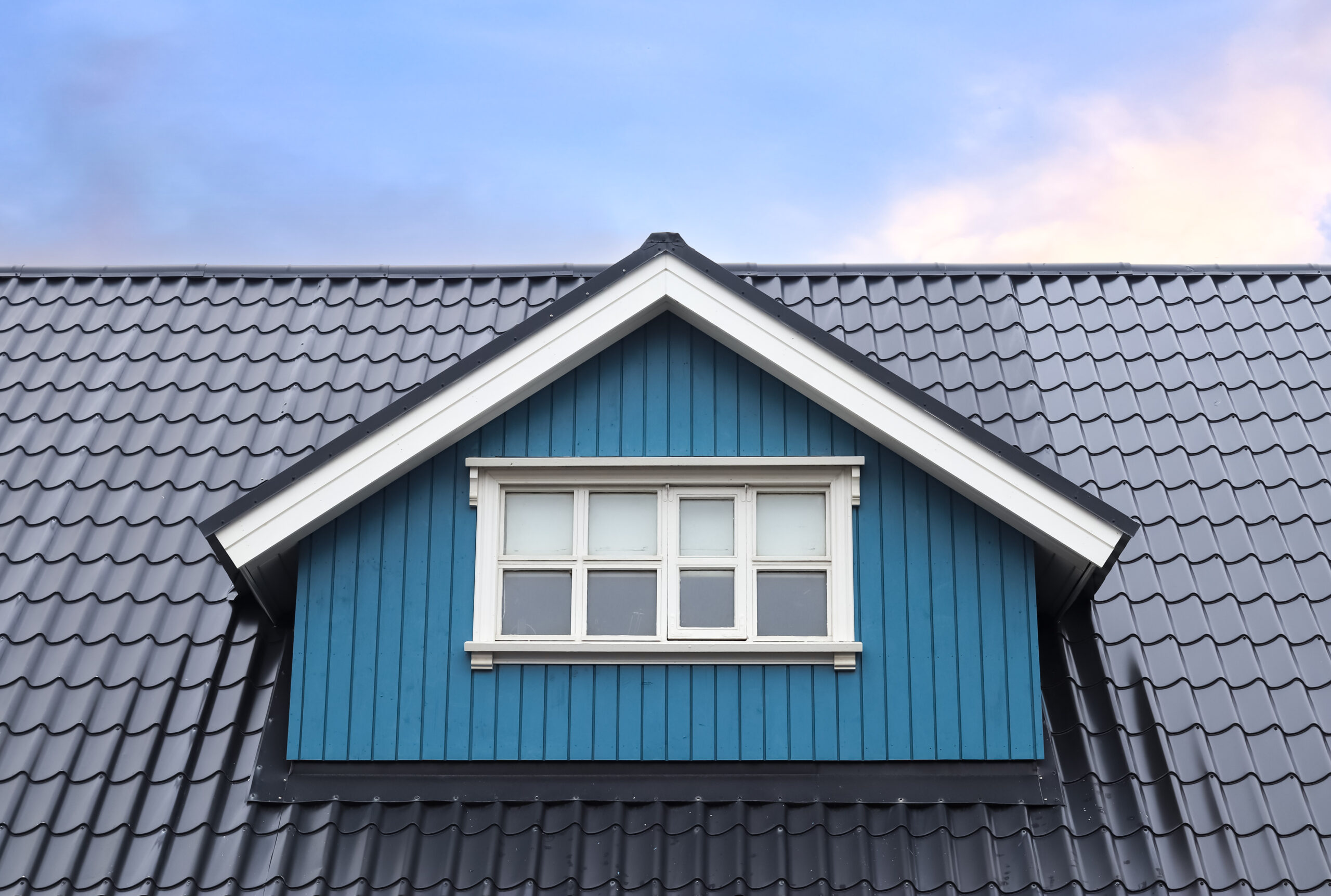 A house that features a beautiful black dormer roof with blue siding near a white-framed window