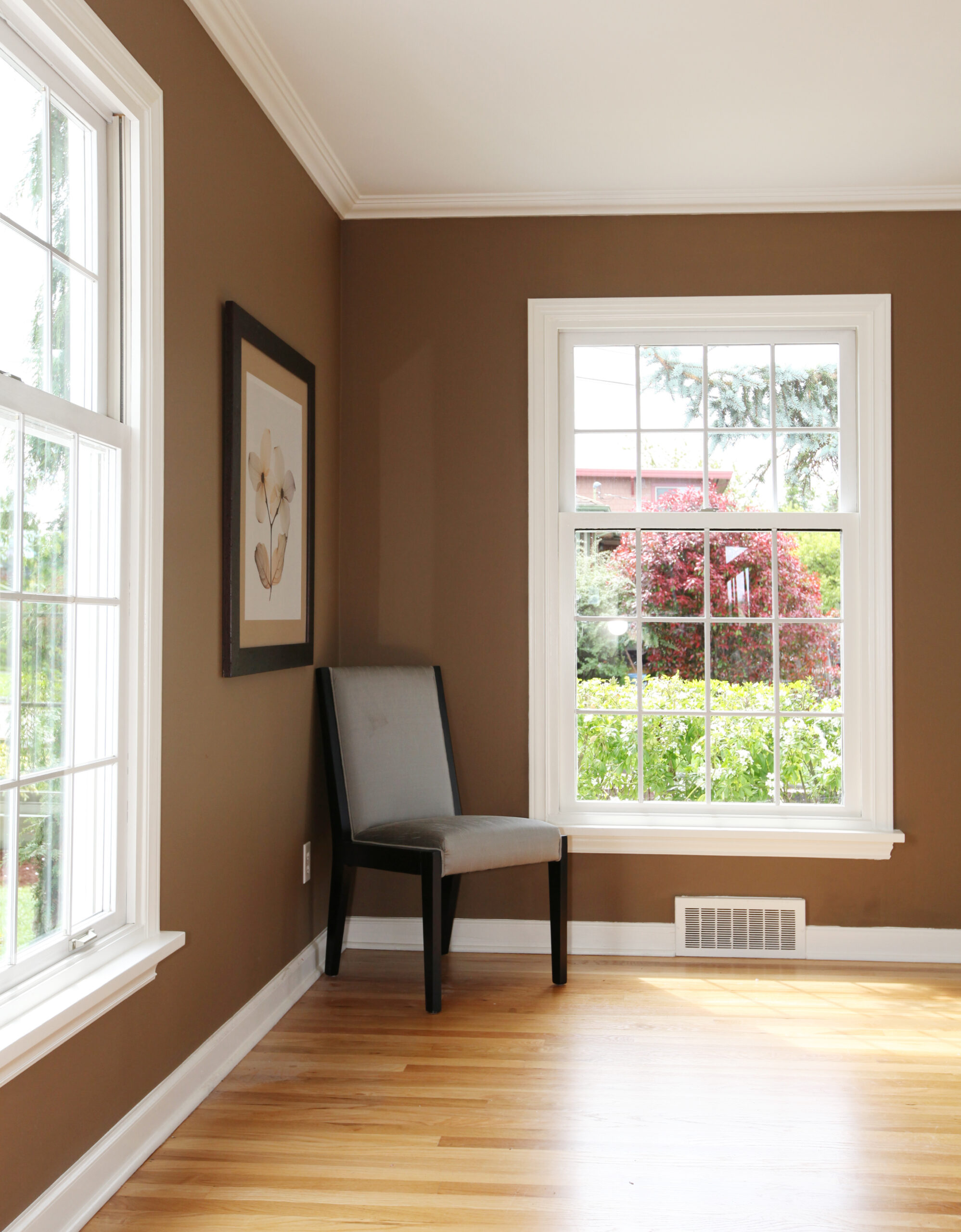 Dining chair tucked in the corner of a room with rich brown walls and large, stunning vinyl windows letting in natural light