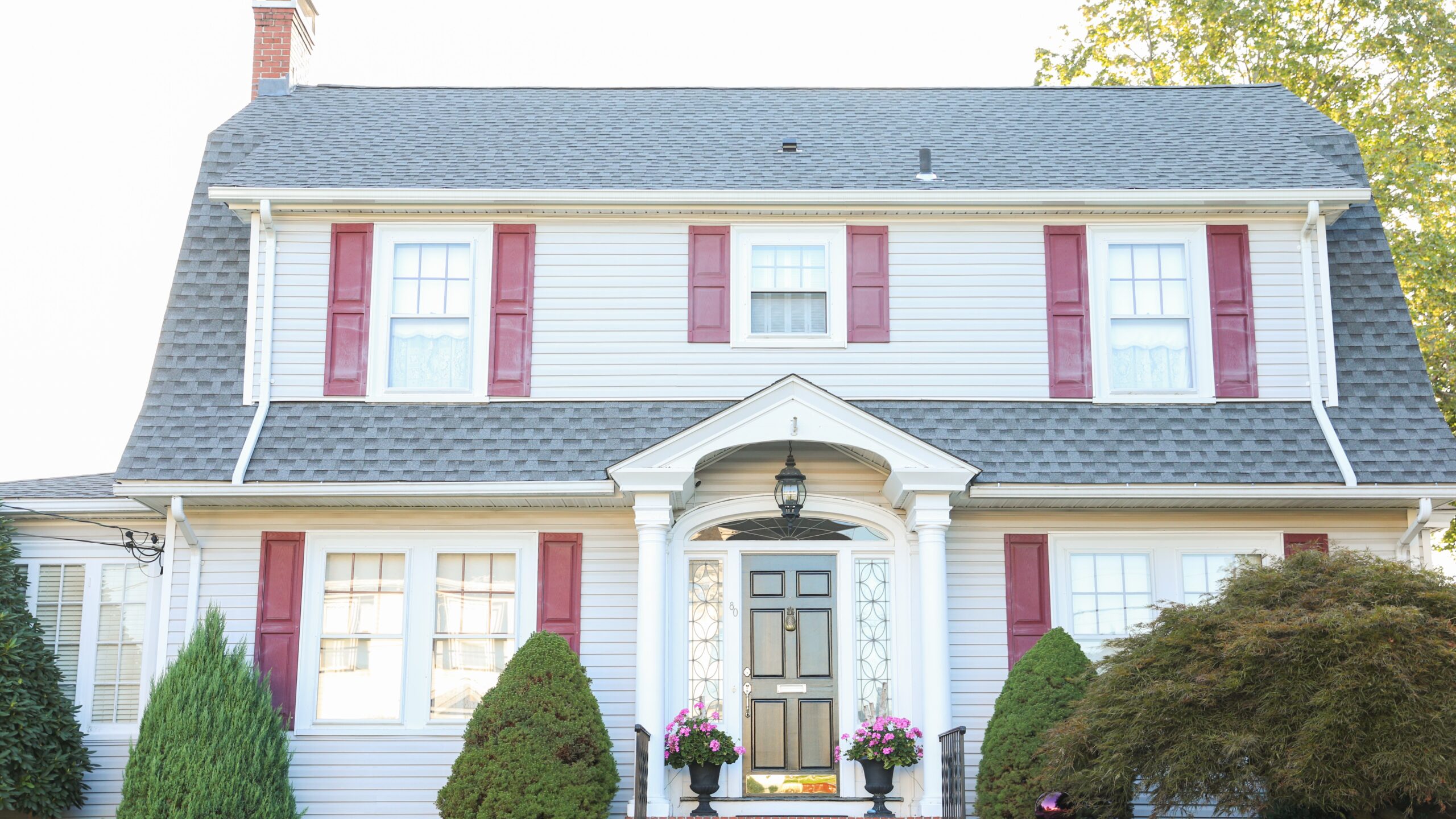 Home with white siding and red window shutters with a big asphalt shingle roof