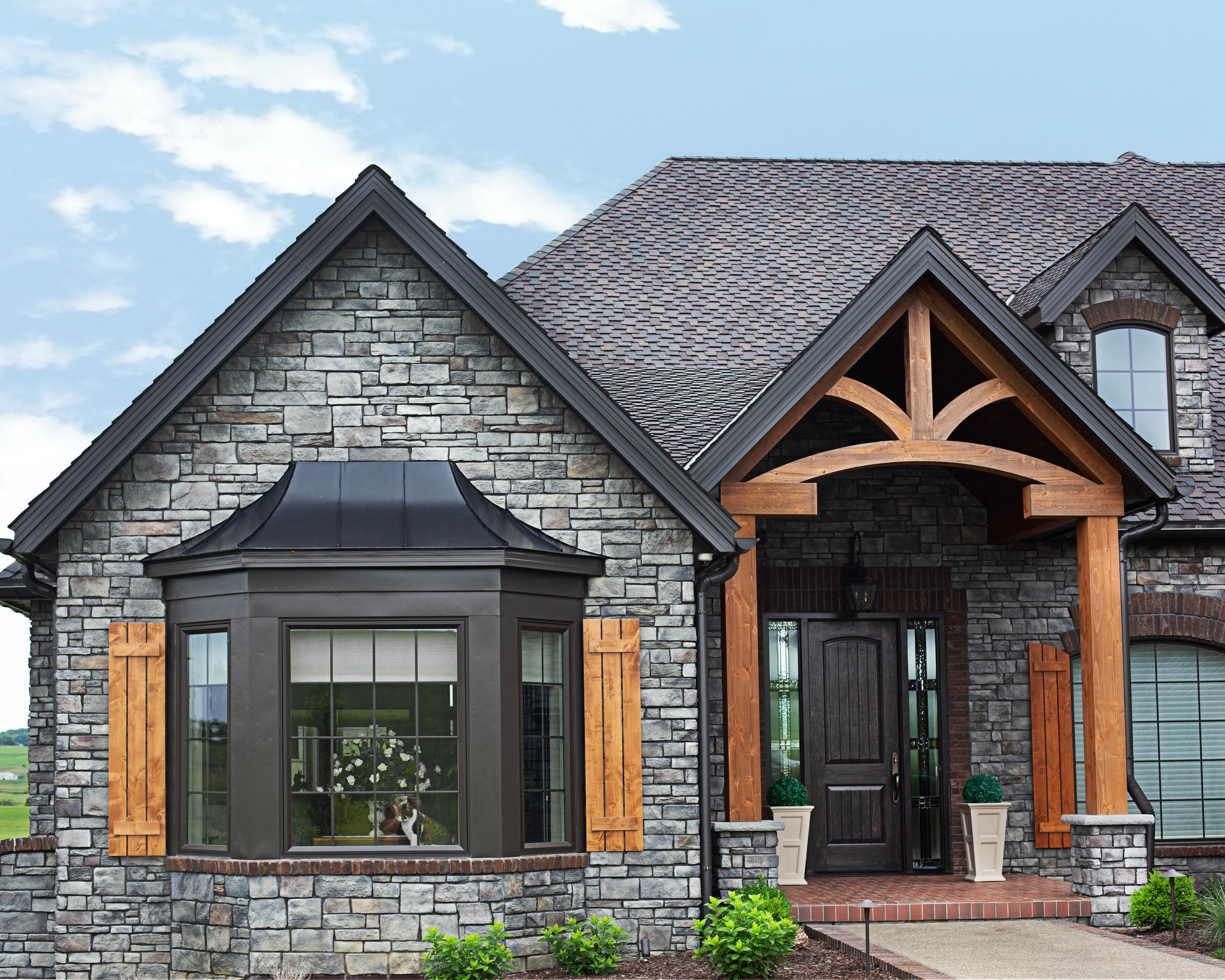 Black by window on a stone house with a shingle roof