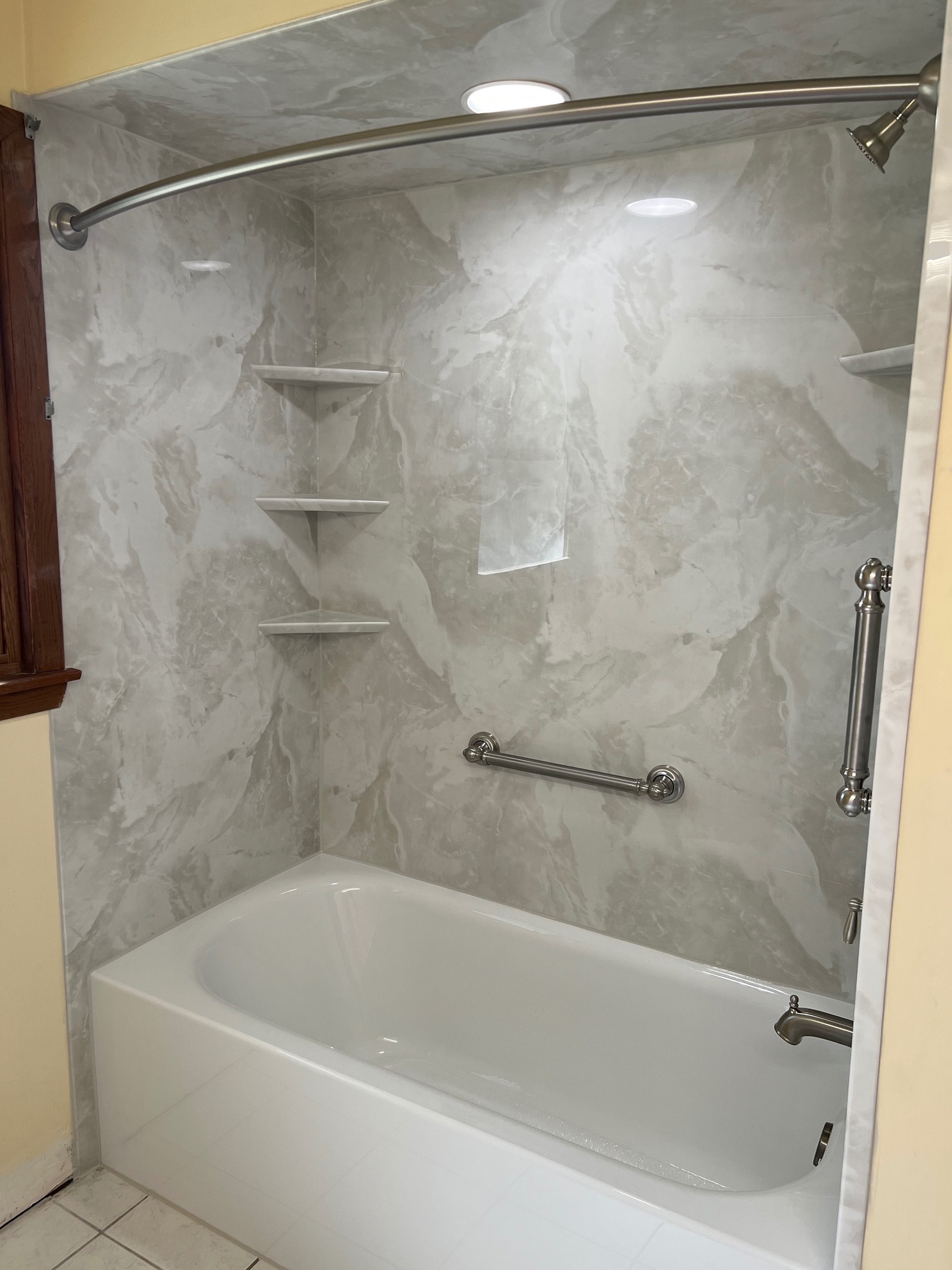 White bathtub with a green surround and silver features with a handrail and built-in shelves